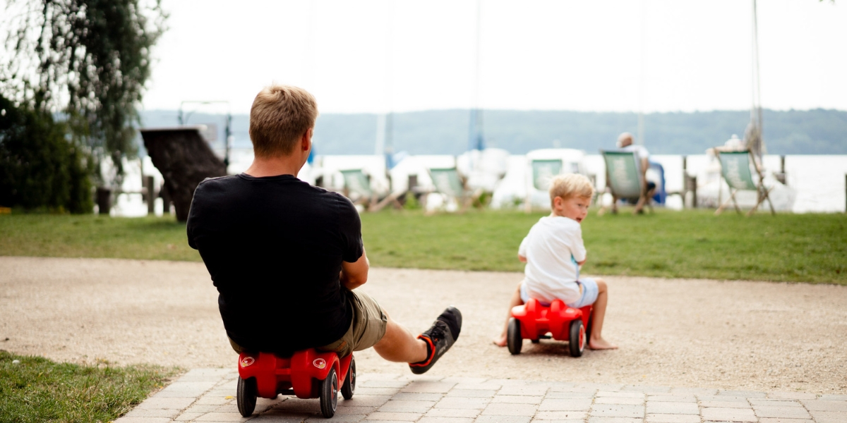 Vater und Sohn fahren mit Spielzeugautos auf dem Weg direkt zur Freiluftbar beim Kongresshotel Potsdam am Templiner See.