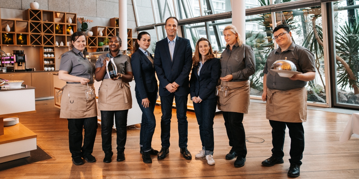 Serviceteam des Kongresshotel Potsdam im Zeppelin-Restaurant mit Requisiten in der Hand. Gläser für Wein. Klosche für Zimmerservice.