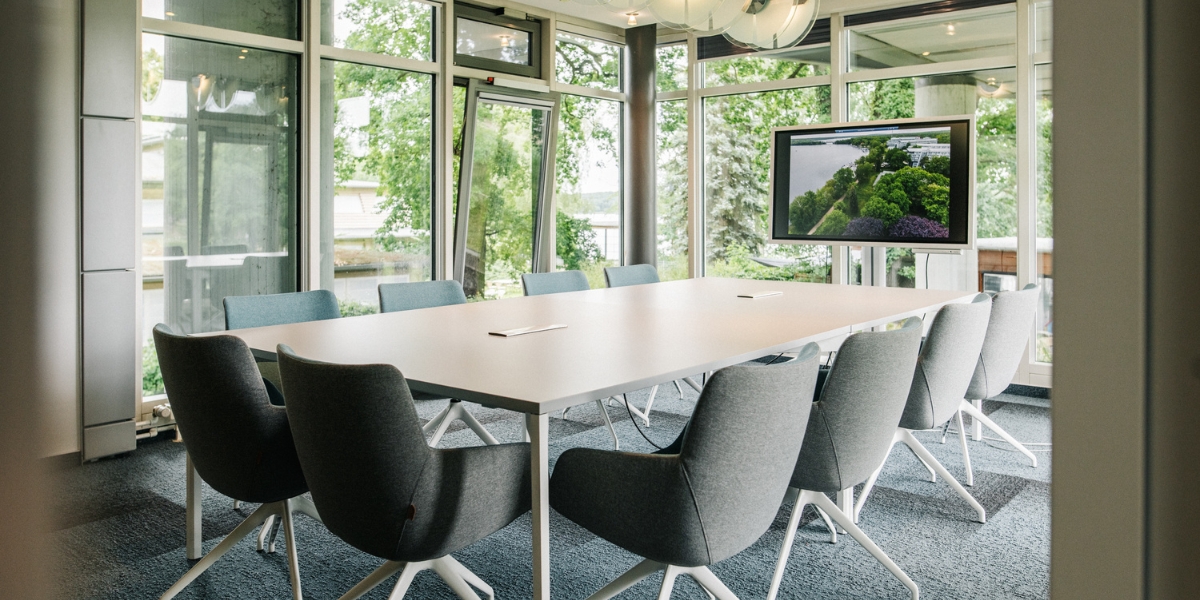 Kreativ Lounge Seeblick im Kongresshotel Potsdam. Ein großer Tisch und Stühle, ein Blick durch die Glaswände auf den Eventgarten, dieFreiluftbar am Templiner See und das Regattahaus.