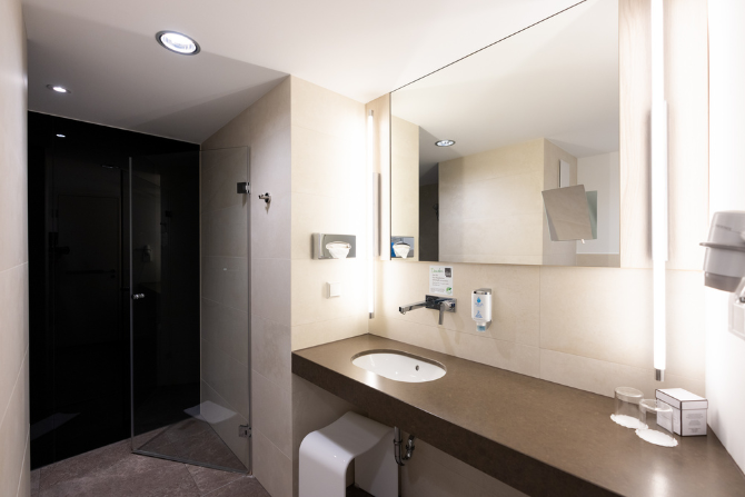 Modernes Hotelbad im Kongresshotel Potsdam mit ebenerdiger Dusche und großem Spiegel.
