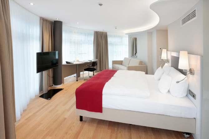 Helle Deluxe Junior Suite im Kongresshotel Potsdam mit Seeblick, Doppelbett und Sitzecke.