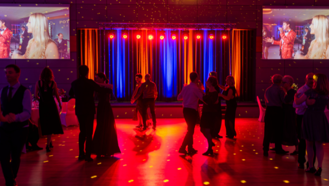 Tanzende Gäste vor einer beleuchteten Bühne mit bunten Lichtern und Bildschirmen.