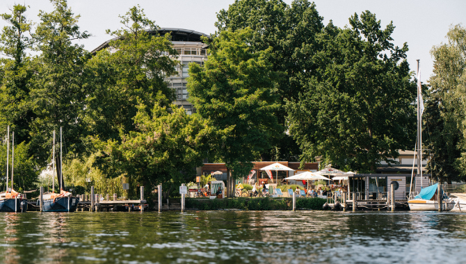 Kongresshotel Potsdam am See mit Terrasse, Bootssteg und Gästen im Grünen