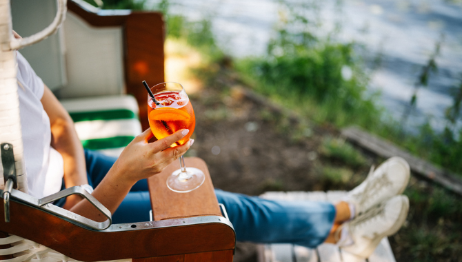 Person im Strandkorb mit Aperol Spritz und Blick auf den See