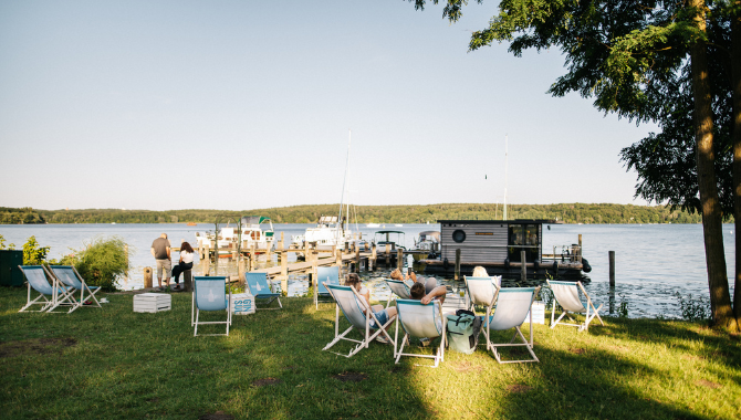 Liegestühle auf einer Wiese am See mit Menschen und Bootssteg