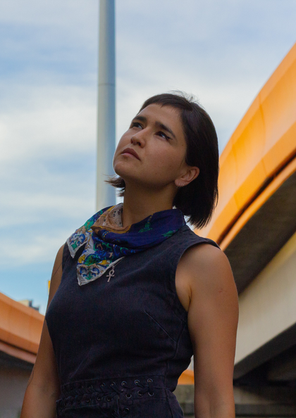 Frau mit Halstuch blickt nachdenklich in den Himmel vor moderner Architektur.